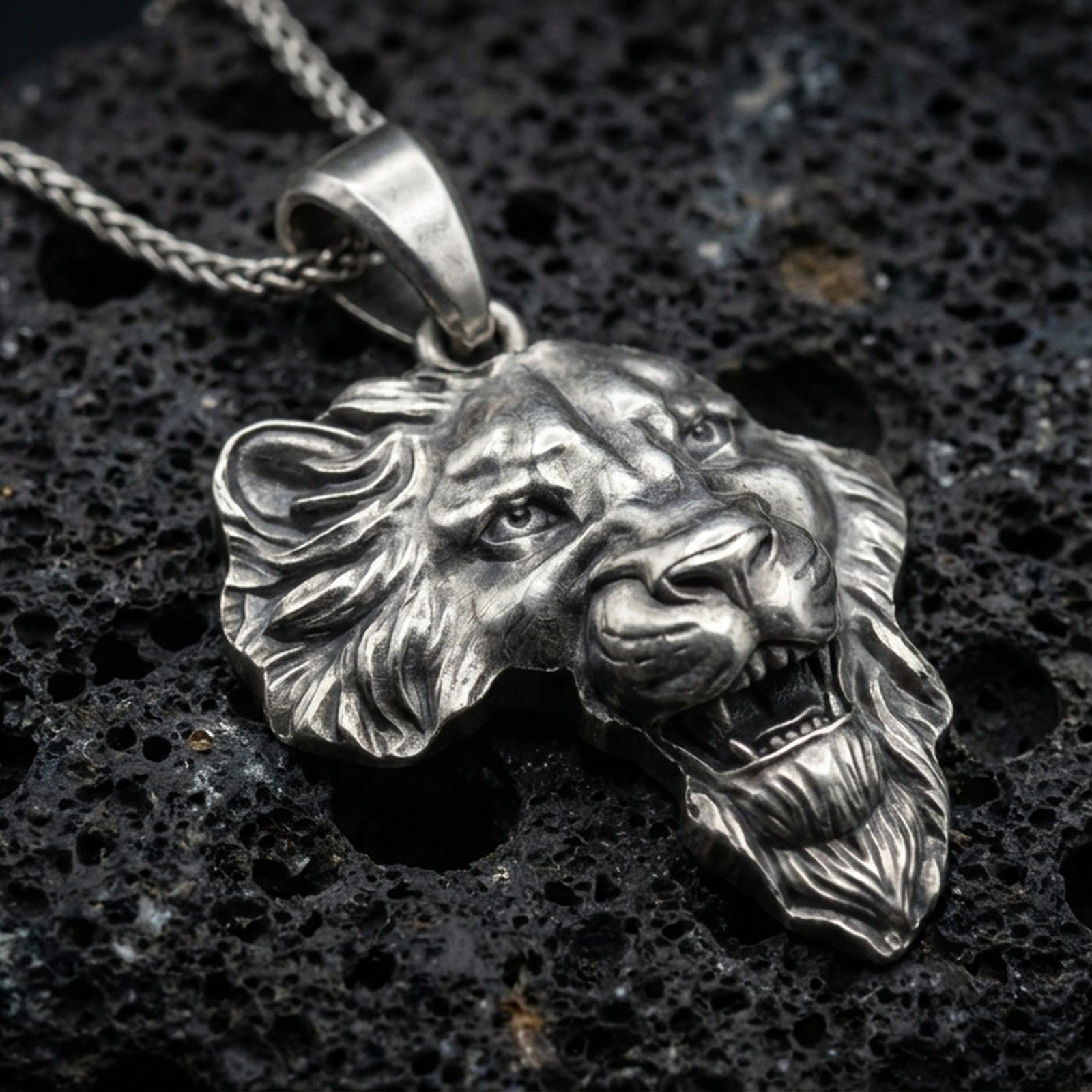 Sterling silver lion head pendant necklace with an oxidized finish resting on textured volcanic rock, captured in a close-up premium studio composition.