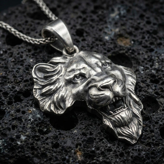 Sterling silver lion head pendant necklace with an oxidized finish resting on textured volcanic rock, captured in a close-up premium studio composition.