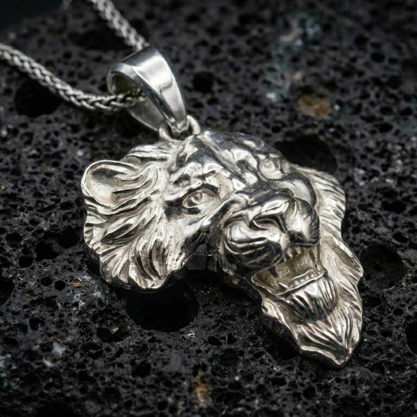 Polished silver lion head pendant necklace displayed on black volcanic rock, shown in a refined macro product shot with detailed mane and facial sculpting.