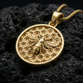 Load image into Gallery viewer, Gold plated bee pendant necklace presented on porous volcanic rock, highlighting the circular medallion form and sculpted insect motif in a luxurious close-up jewelry image.
