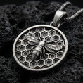 Load image into Gallery viewer, Sterling silver bee pendant necklace with an oxidized finish resting on textured volcanic rock, captured in a close-up premium studio composition.
