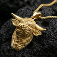 Load image into Gallery viewer, Gold plated buffalo head pendant necklace presented on porous volcanic rock, highlighting the rustic animal design in a luxurious close-up jewelry image.
