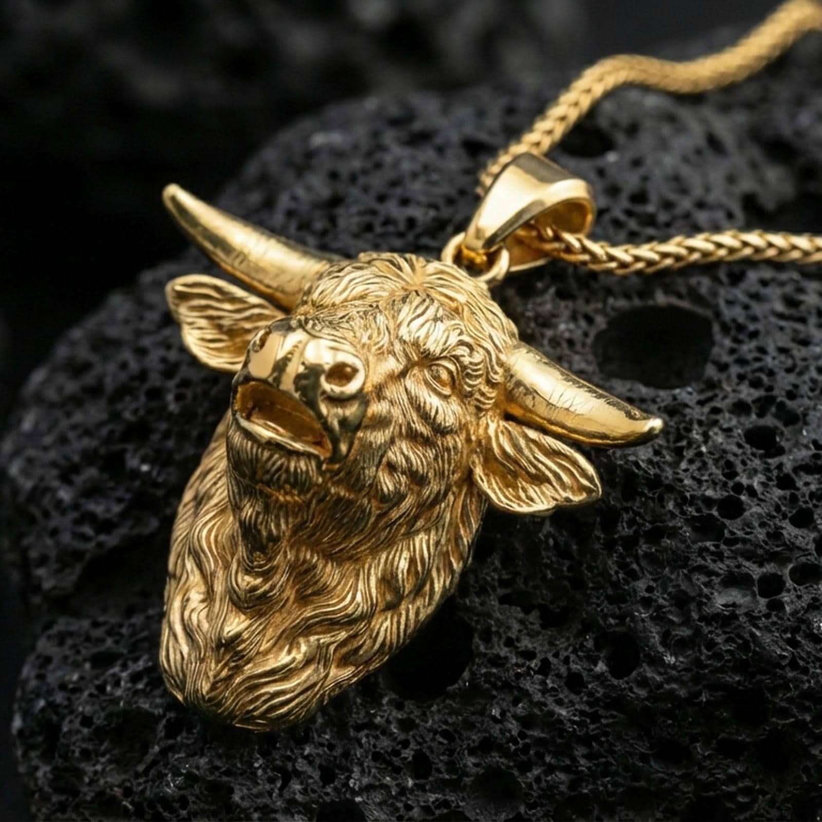 Gold plated buffalo head pendant necklace presented on porous volcanic rock, highlighting the rustic animal design in a luxurious close-up jewelry image.