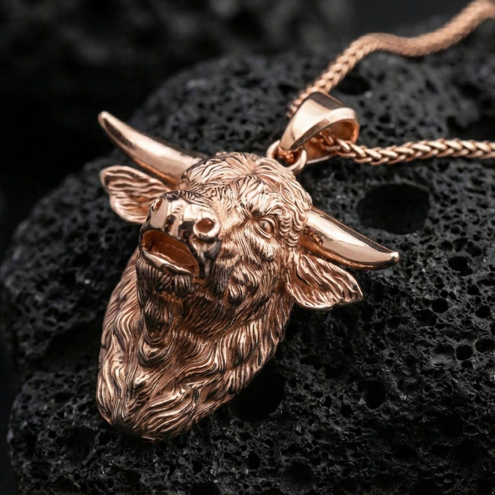 Rose gold plated buffalo head pendant necklace on dark volcanic rock, photographed in a detailed premium studio macro view.