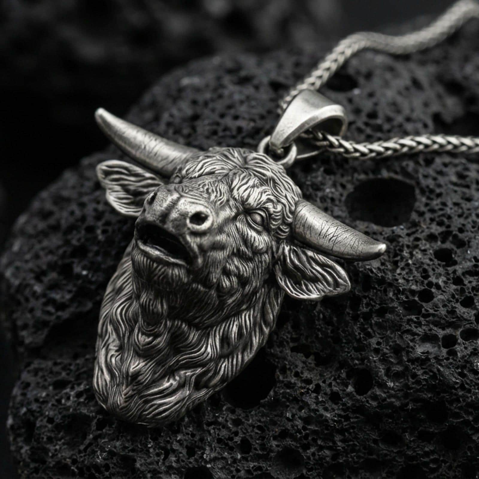 Sterling silver buffalo head pendant necklace with an oxidized finish resting on textured volcanic rock, captured in a close-up premium studio composition.