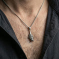 Load image into Gallery viewer, Oxidized hanging bat pendant necklace worn on the neck, styled in a dark lifestyle portrait with an open shirt and masculine presentation.

