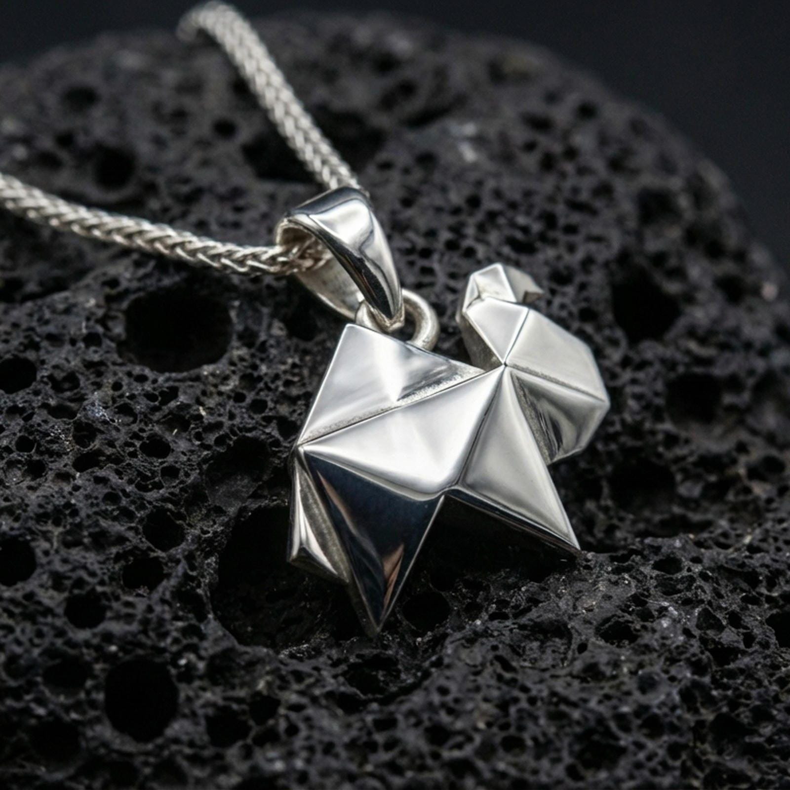 Polished silver origami camel pendant necklace displayed on black volcanic rock, shown in a refined macro product shot with crisp folded geometric detail.