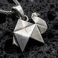 Load image into Gallery viewer, Sterling silver origami camel pendant necklace with an oxidized finish resting on textured volcanic rock, captured in a close-up premium studio composition.
