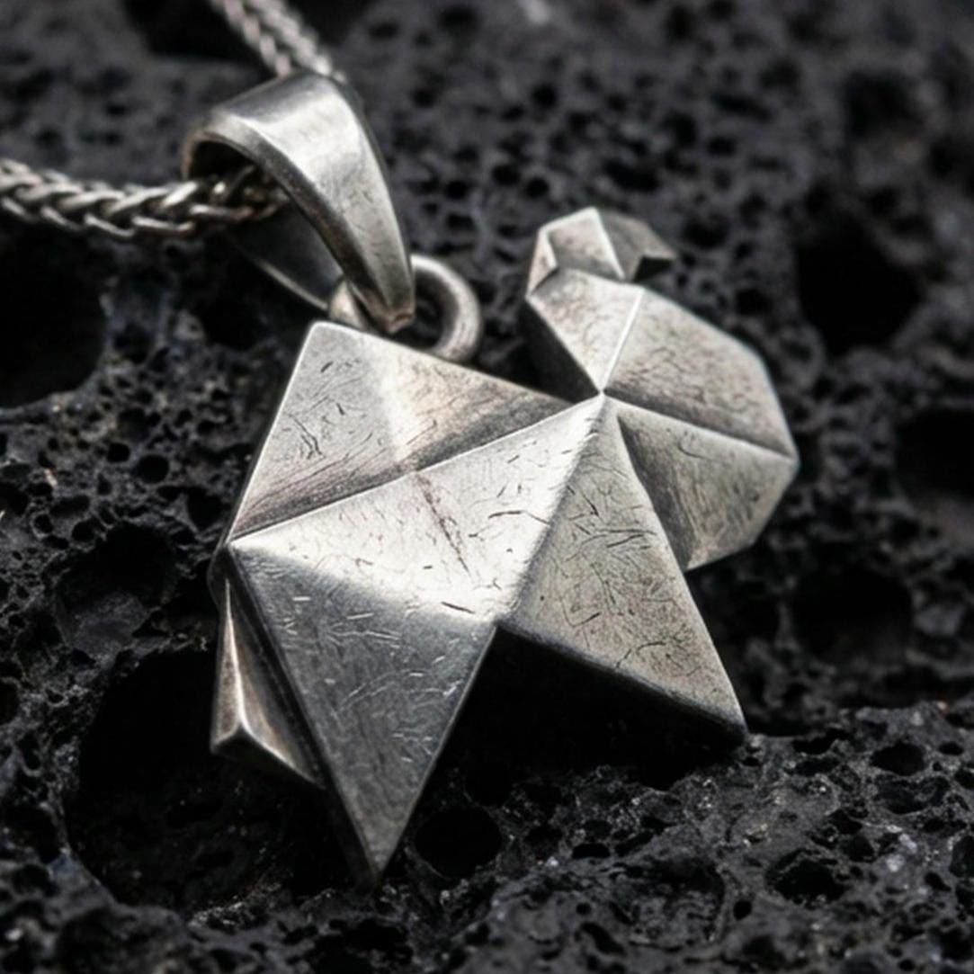 Sterling silver origami camel pendant necklace with an oxidized finish resting on textured volcanic rock, captured in a close-up premium studio composition.