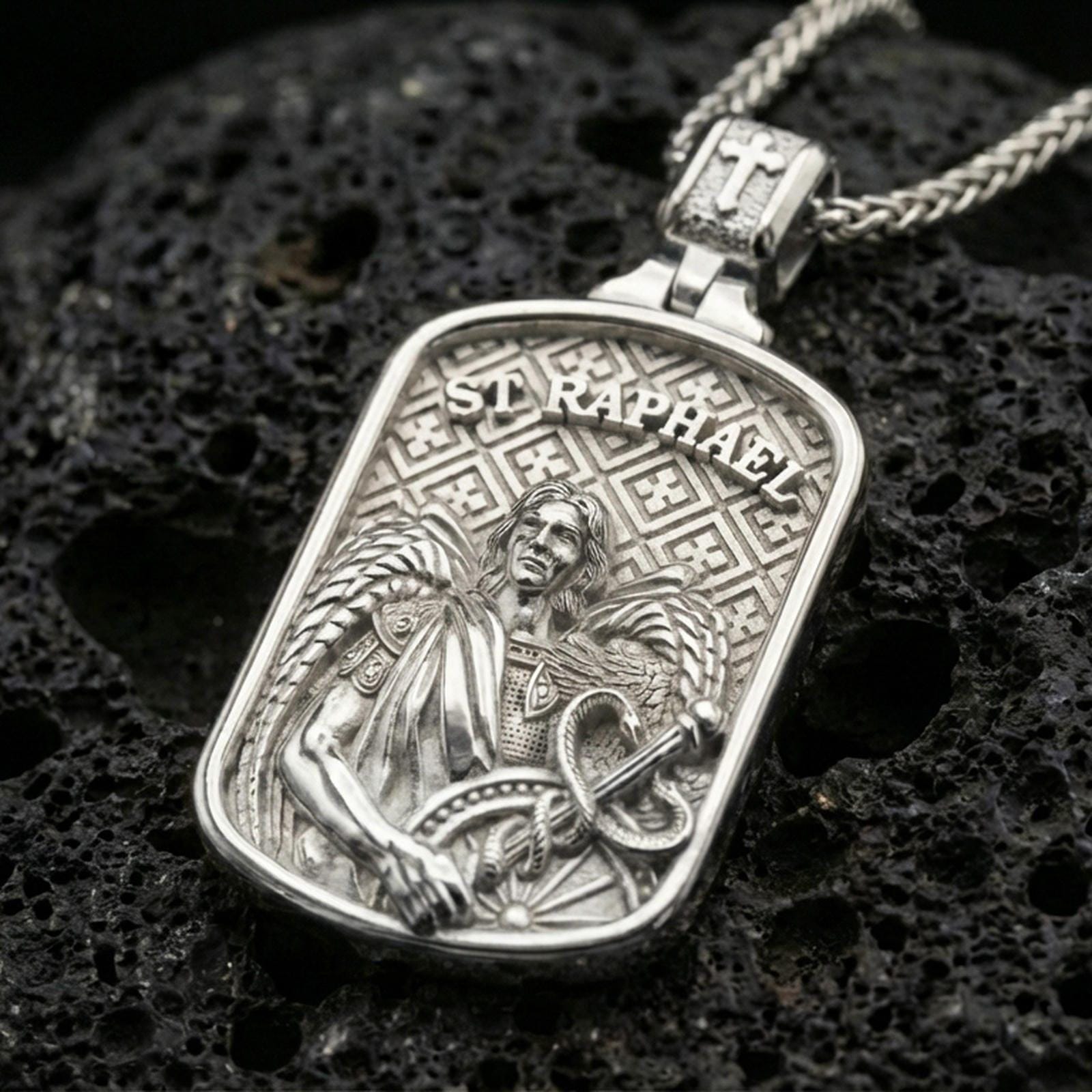 Polished 925 sterling silver St Raphael medal pendant on black volcanic stone, showing crisp archangel engraving.