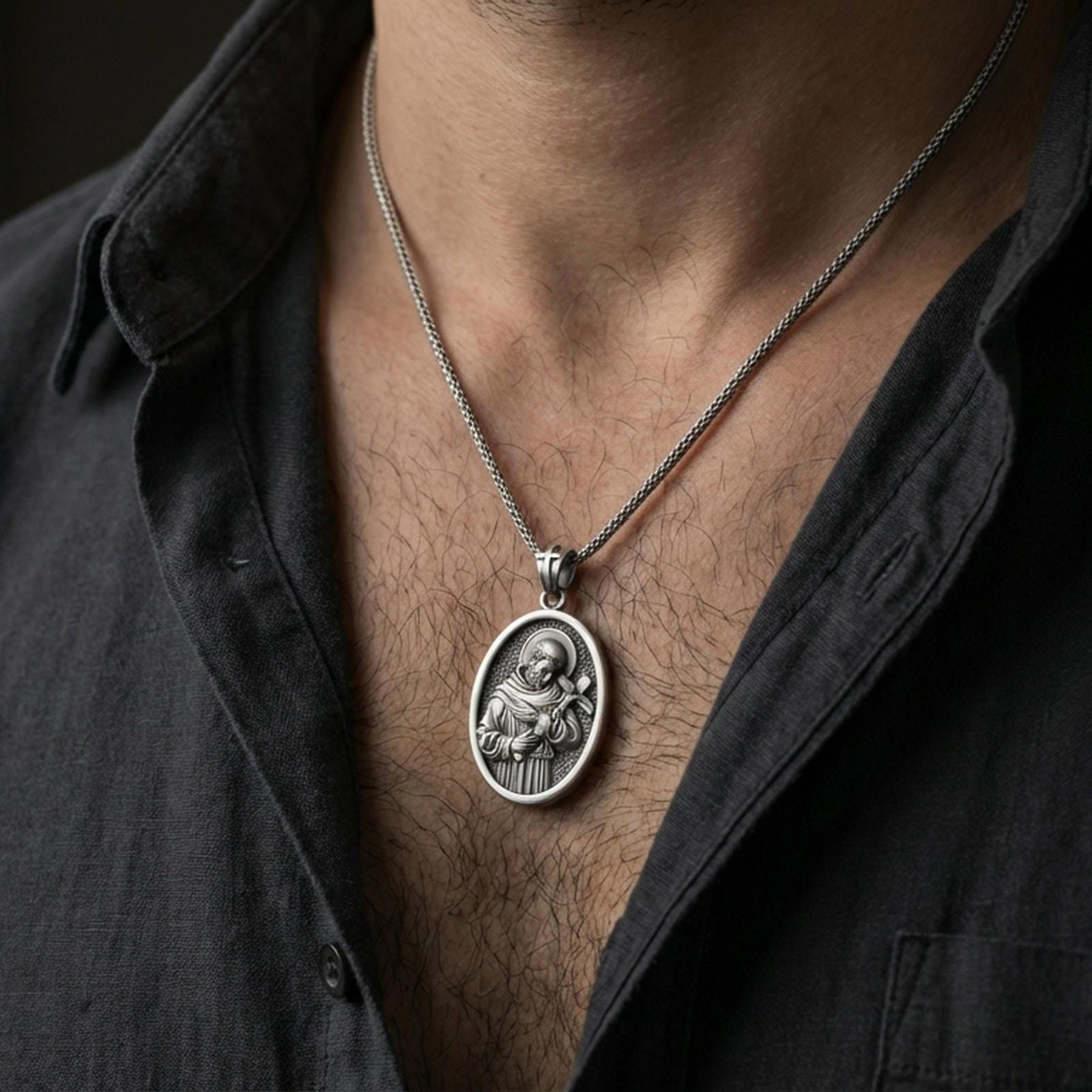 Oxidized Saint Francis pendant with halo and cross worn on the neck in a lifestyle jewelry shot, styled against the chest for a devotional and timeless look
