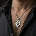 Load image into Gallery viewer, Polished silver Saint Francis medallion with detailed saint relief worn on the neck in a close lifestyle frame, highlighting the halo, cross, and sacred symbolism
