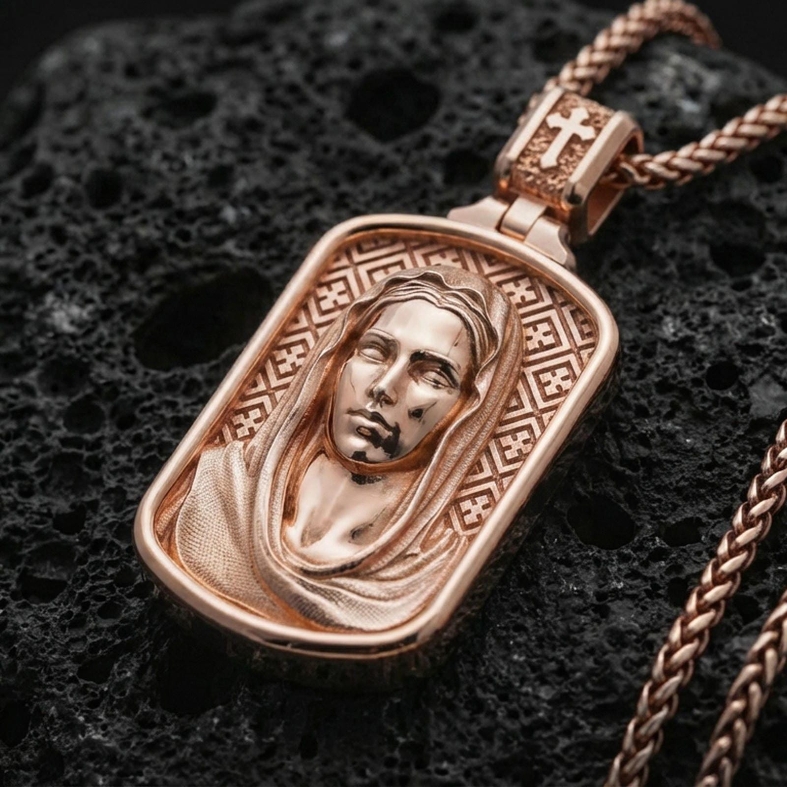Rose gold plated Madonna pendant with veiled female figure, soft devotional expression, and framed icon design resting on volcanic rock in an elegant close-up product presentation