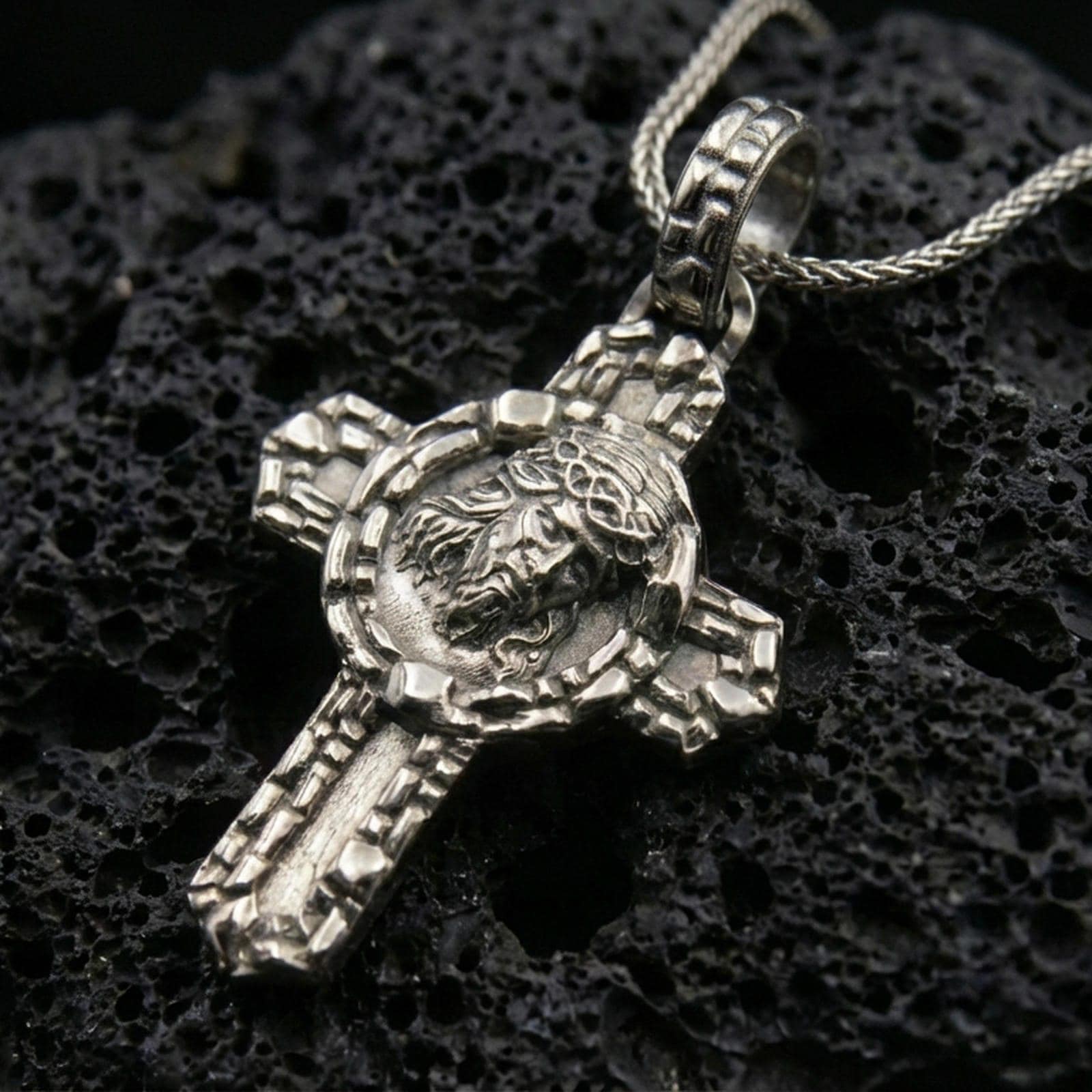 Oxidized 925 sterling silver Jesus crucifix pendant on black volcanic rock with crown of thorns relief.