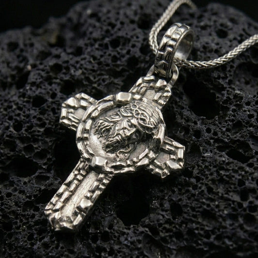 Oxidized 925 sterling silver Jesus crucifix pendant on black volcanic rock with crown of thorns relief.