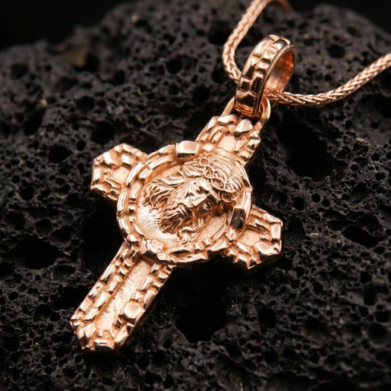 Rose gold plated Christ crucifix necklace on black volcanic stone with ornate Christian cross detailing.