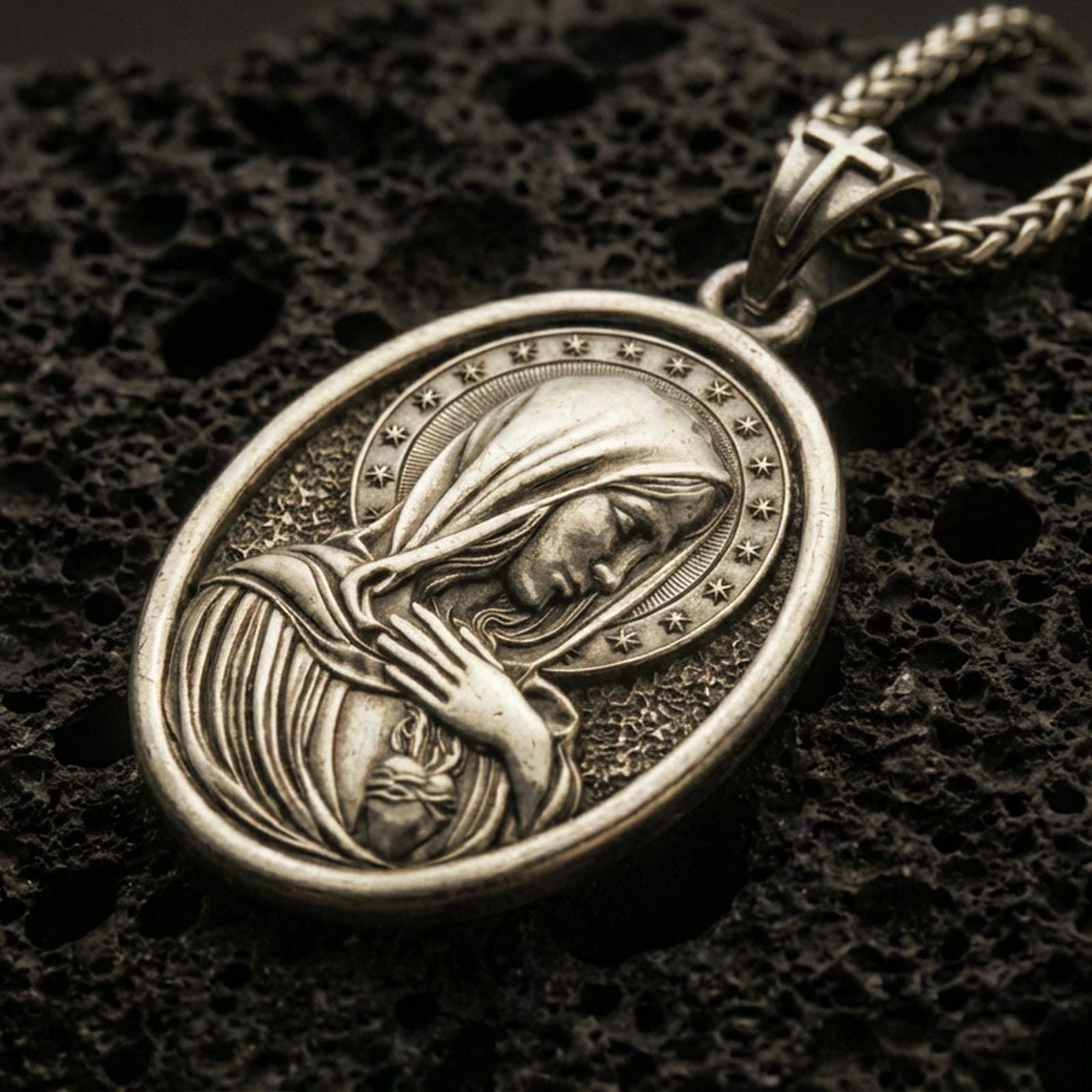 Bronze Immaculate Heart Virgin Mary pendant with halo of stars and devotional portrait displayed on dark volcanic rock in a close-up luxury jewelry composition