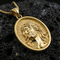 Load image into Gallery viewer, Gold plated Jesus Christ pendant with crown of thorns, flowing hair detail, and oval medallion design showcased on black volcanic rock in a refined macro jewelry image
