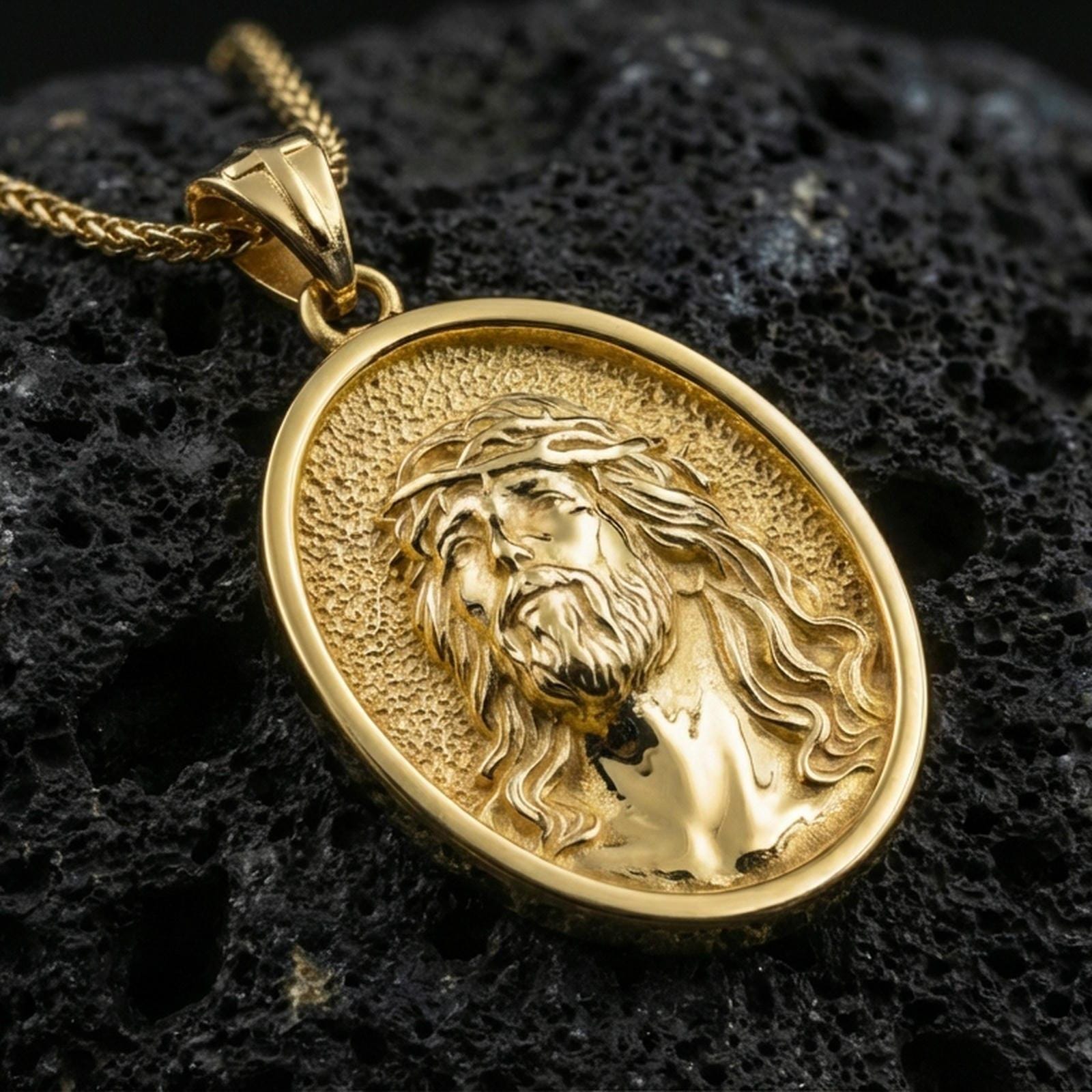 Gold plated Jesus Christ pendant with crown of thorns, flowing hair detail, and oval medallion design showcased on black volcanic rock in a refined macro jewelry image