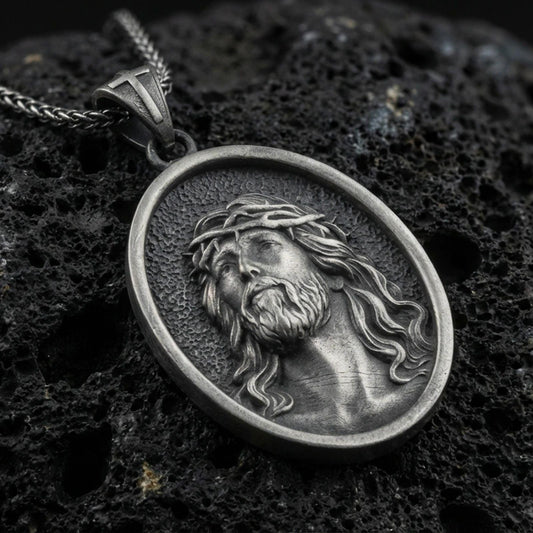 Oxidized Jesus Christ pendant with crown of thorns and detailed sacred portrait displayed on dark volcanic rock in a close-up luxury jewelry composition