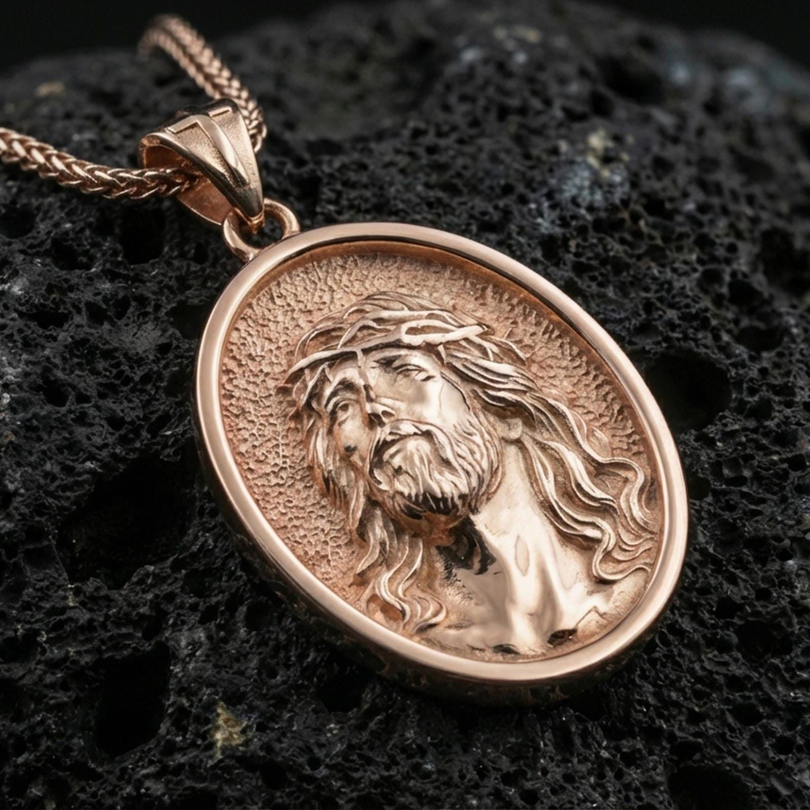Rose gold plated religious Jesus medal with detailed crown of thorns portrait and smooth oval silhouette resting on volcanic rock in an elegant close-up product presentation