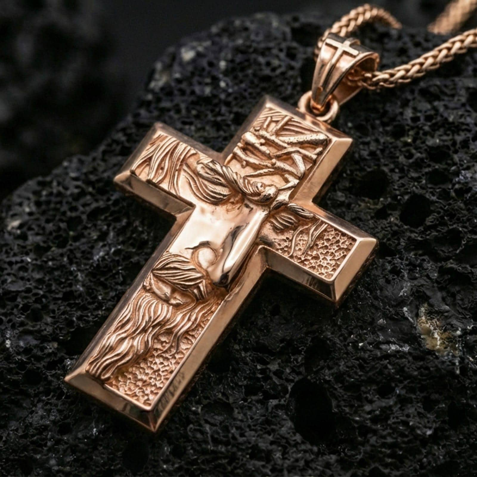 Rose gold plated religious cross pendant with sculpted Jesus figure, crown of thorns, and classic crucifix silhouette resting on volcanic rock in an elegant close-up product presentation