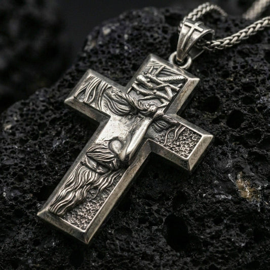 Oxidized Jesus cross pendant with sculpted crucifix figure, crown of thorns, and textured relief displayed on dark volcanic rock in a close-up luxury jewelry composition