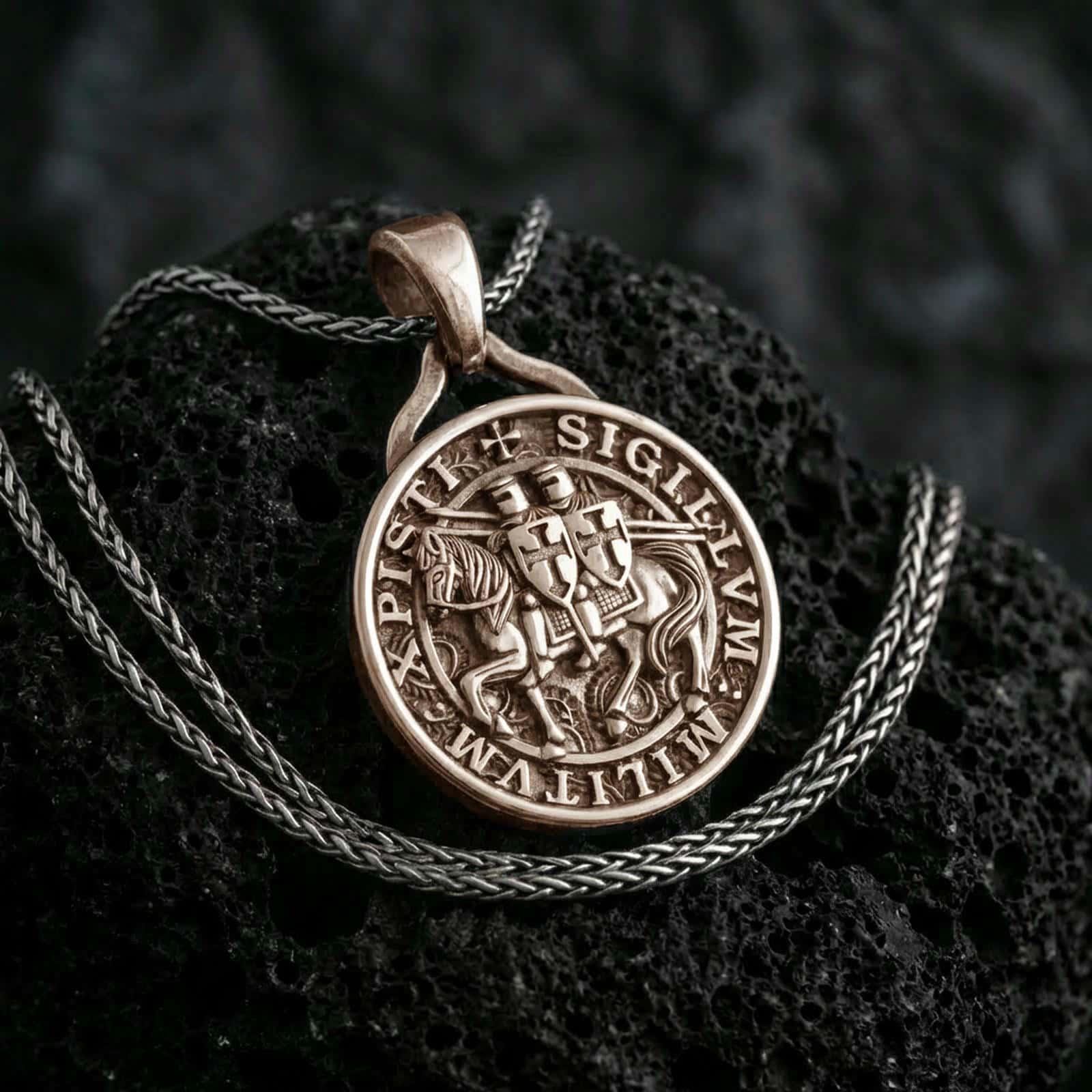 Bronze Knights Templar seal pendant necklace with an oxidized finish resting on textured volcanic rock, captured in a close-up premium studio composition.