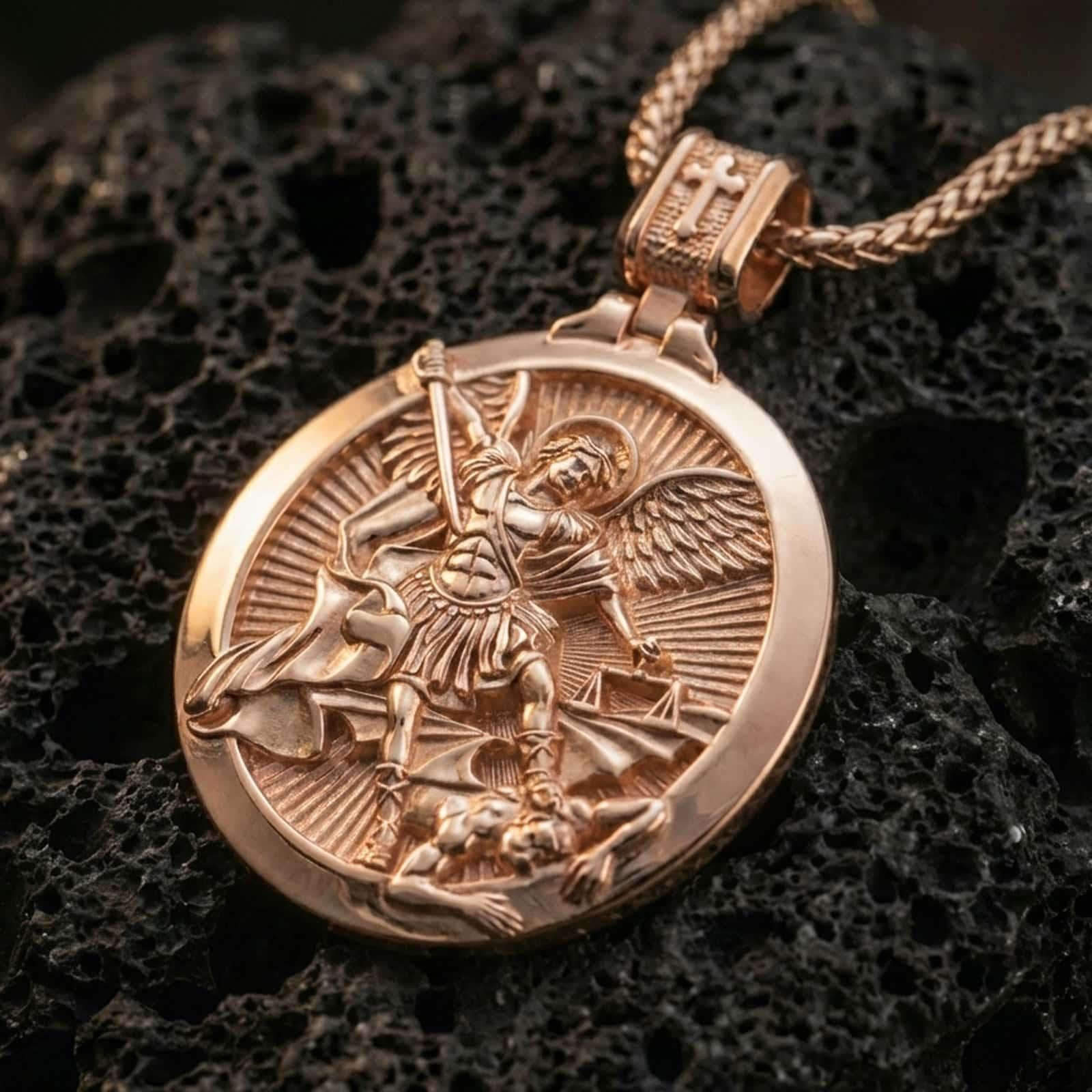 Rose gold plated Saint Michael pendant necklace on dark volcanic rock, photographed in a detailed premium studio macro view.