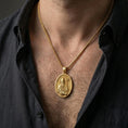 Load image into Gallery viewer, Gold plated Saint Patrick pendant necklace worn on the neck, captured on a human model in a premium dark-toned lifestyle frame.
