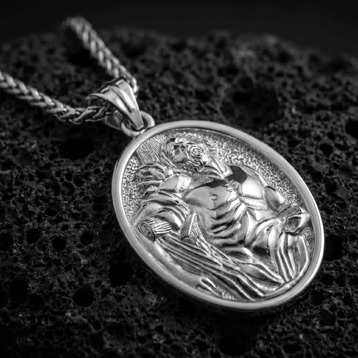 Polished silver Saint Sebastian pendant necklace displayed on black volcanic rock, shown in a refined macro product shot with detailed martyr figure relief.