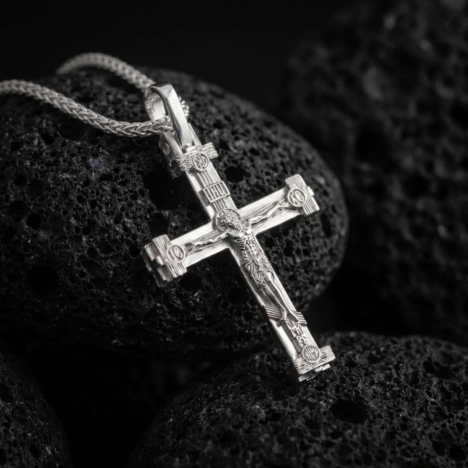 Polished silver Orthodox cross pendant necklace displayed on black volcanic rock, shown in a refined macro product shot with detailed crucifix figure and Slavonic inscription accents.