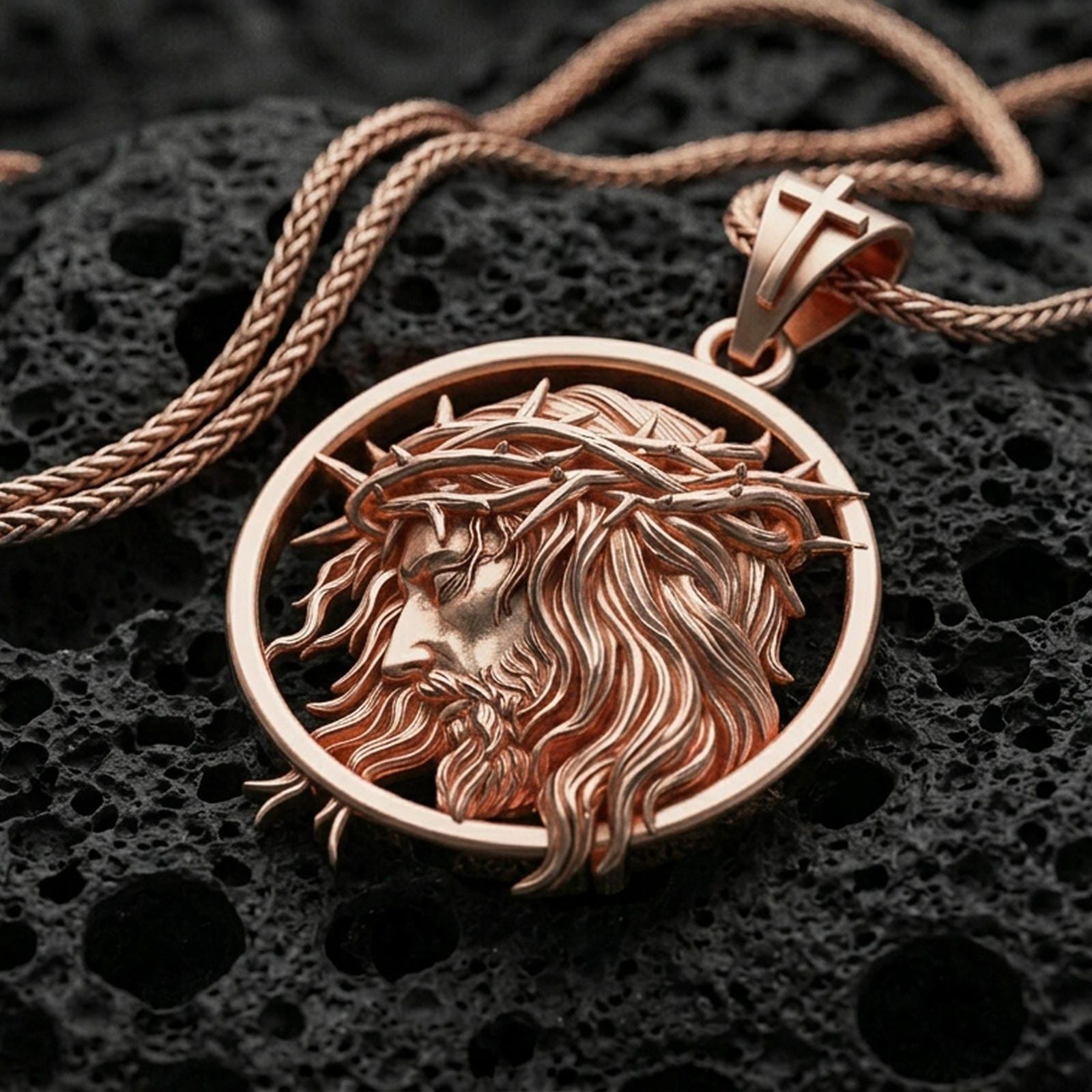 Rose gold plated religious Jesus pendant with flowing hair, crown of thorns, and circular portrait design resting on volcanic rock in an elegant close-up product presentation