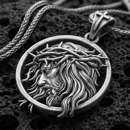Oxidized Jesus crown of thorns pendant with side profile portrait and flowing hair detail displayed on dark volcanic rock in a close-up luxury jewelry composition