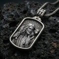 Load image into Gallery viewer, Oxidized Good Shepherd Jesus pendant with lamb over the shoulders and framed devotional portrait displayed on dark volcanic rock in a close-up luxury jewelry composition
