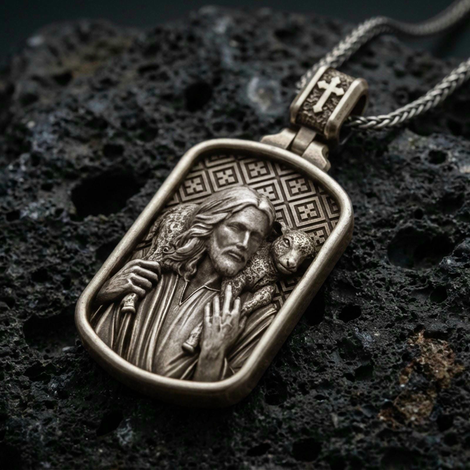 Bronze Good Shepherd Jesus pendant with lamb over the shoulders and framed devotional portrait displayed on dark volcanic rock in a close-up luxury jewelry composition