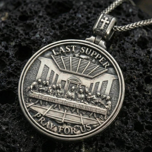 Oxidized Last Supper pendant with Pray for Us inscription, detailed round medallion design, and two-sided devotional concept displayed on dark volcanic rock in a close-up luxury jewelry composition