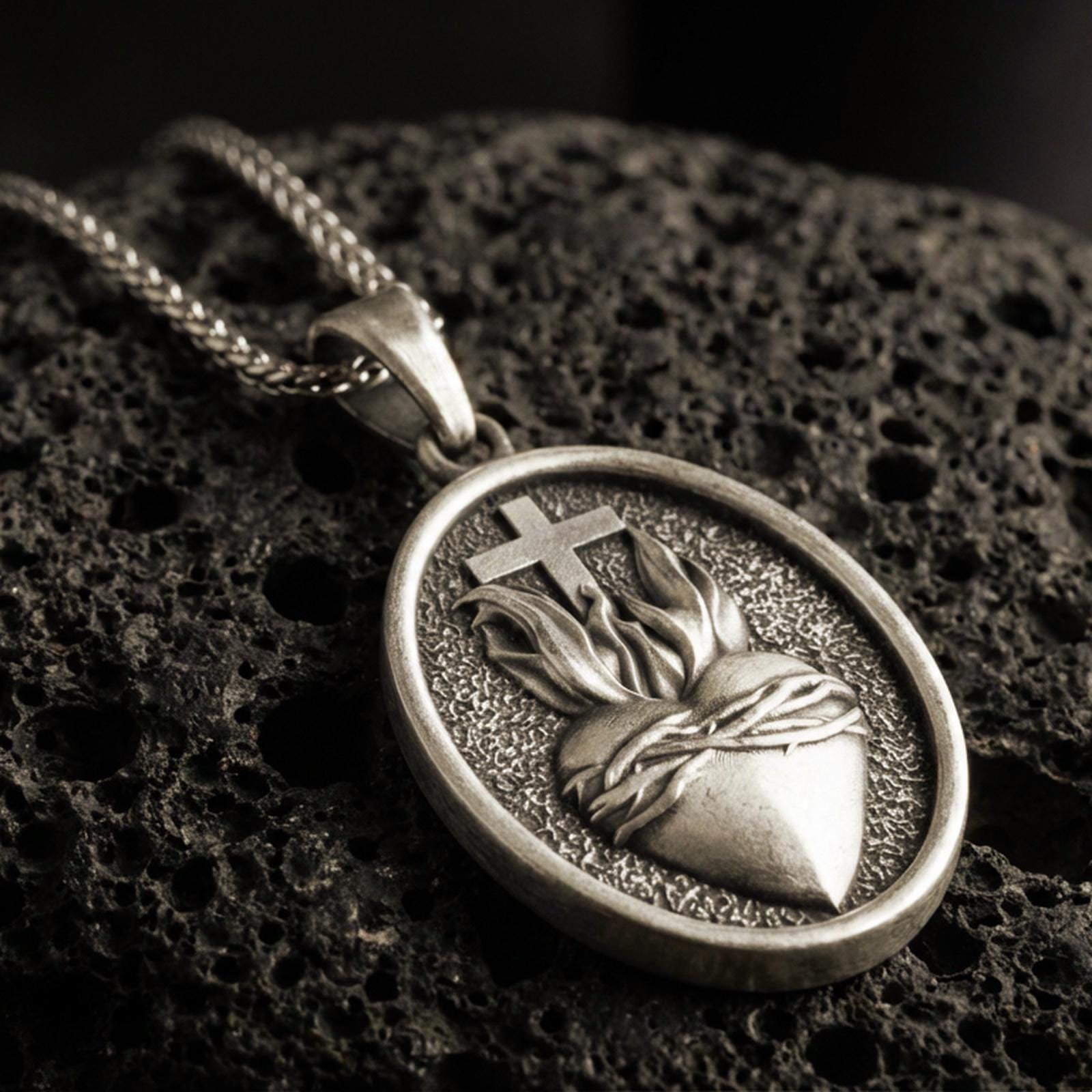 Bronze Sacred Heart pendant with cross, flame detail, and oval devotional design displayed on dark volcanic rock in a close-up luxury jewelry composition