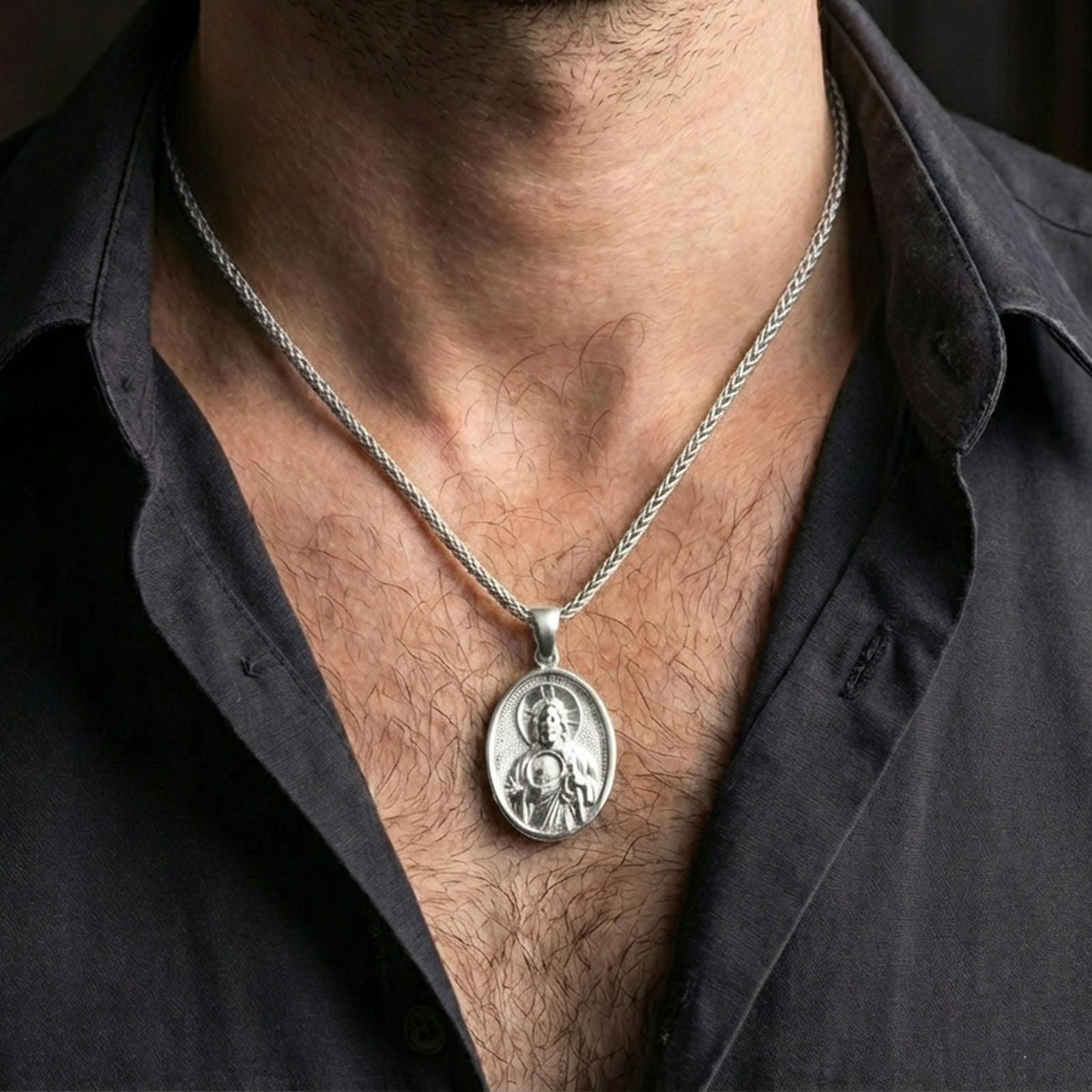 Polished silver Saint Jude medal with sacred portrait relief worn on the neck in a close lifestyle frame, highlighting the oval silhouette and refined saint detail