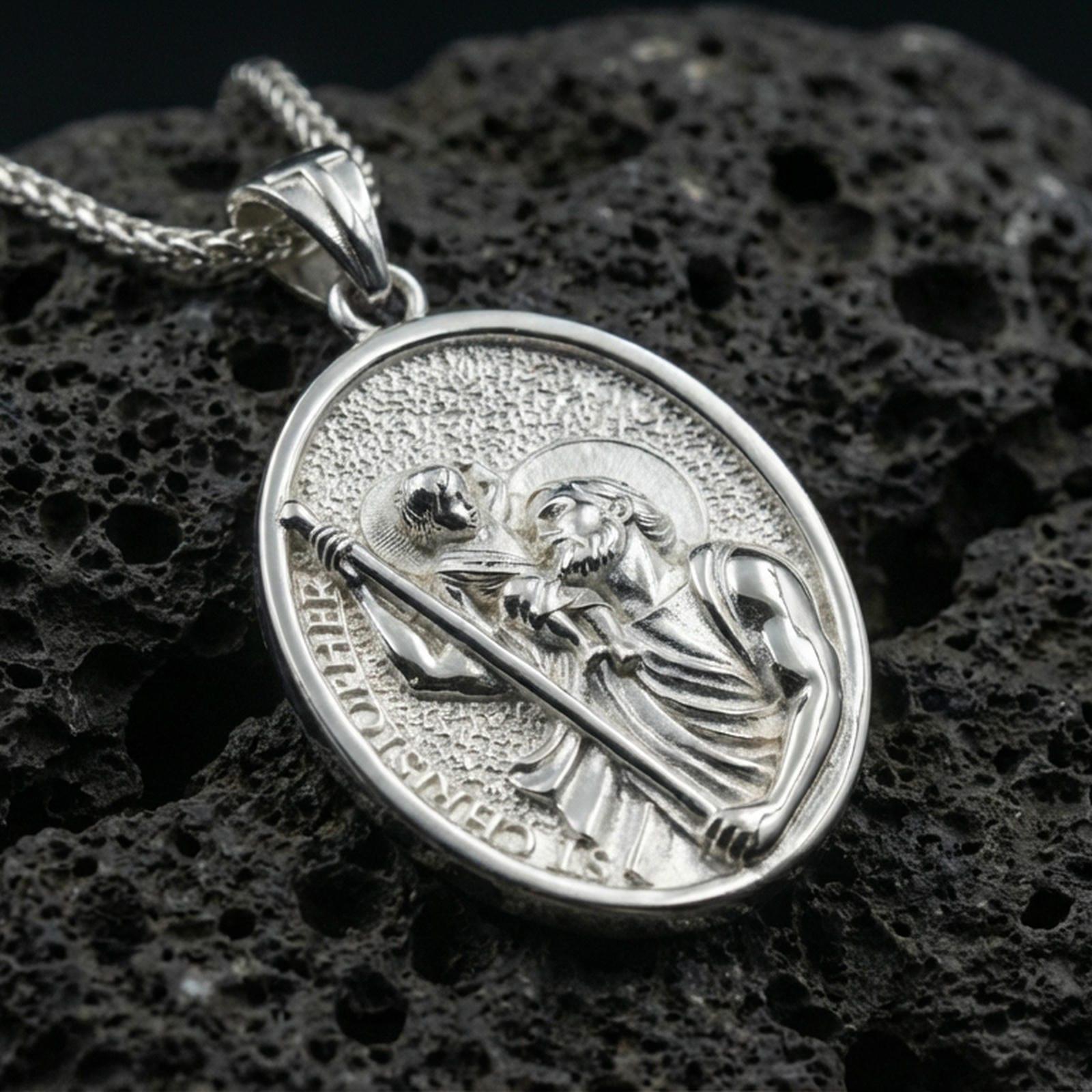 Polished silver Saint Christopher medal with detailed saint relief, Child Jesus figure, and engraved devotional lettering placed on textured volcanic rock in a premium studio product shot
