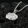 Load image into Gallery viewer, Polished silver chakra necklace with raised Om symbol, geometric triangle detail, and stylized lotus form placed on textured volcanic rock in a premium studio product shot
