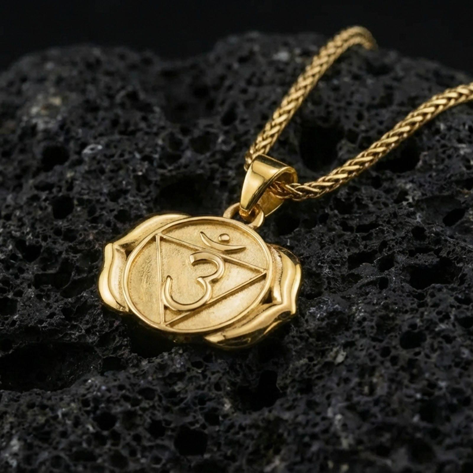 Gold plated third eye chakra pendant with sacred Om motif, symbolic triangular center, and smooth spiritual silhouette showcased on black volcanic rock in a refined macro jewelry image