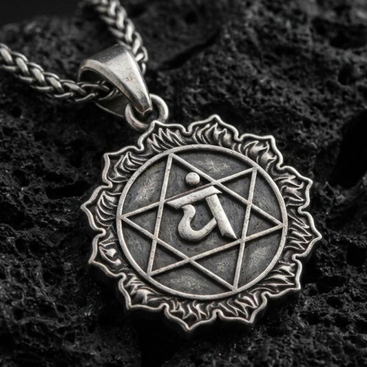 Oxidized Anahata chakra pendant with sacred symbol, hexagram motif, and sunburst border displayed on dark volcanic rock in a close-up luxury jewelry composition
