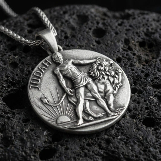 Oxidized Lion of Judah pendant with Judah inscription, lion figure, and sunrise motif displayed on dark volcanic rock in a close-up luxury jewelry composition