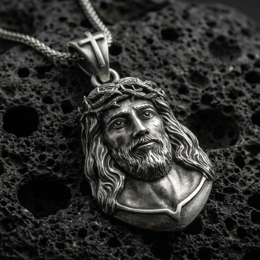 Oxidized Jesus Christ pendant with crown of thorns, sculpted sacred portrait, and detailed facial relief displayed on dark volcanic rock in a close-up luxury jewelry composition