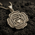 Load image into Gallery viewer, Bronze heart chakra pendant with sacred symbol, geometric frame, and lotus petal border displayed on dark volcanic rock in a close-up luxury jewelry composition
