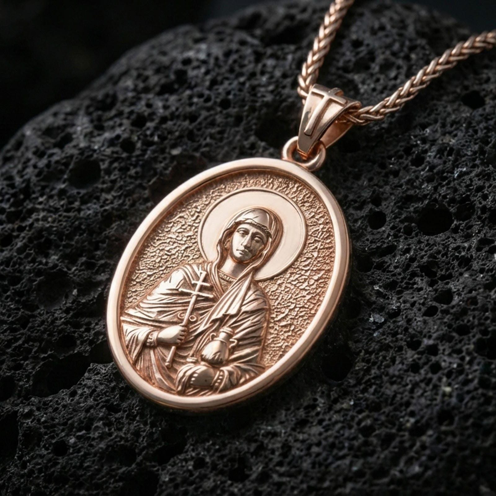 Rose gold plated Orthodox Christian Saint Anastasia necklace with haloed figure, devotional relief, and elegant oval silhouette resting on volcanic rock in an elegant close-up product presentation
