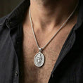 Load image into Gallery viewer, Polished silver Saint Paul medallion with saint relief and halo motif worn on the neck in a close lifestyle frame, highlighting the oval silhouette and sacred detailing
