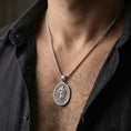 Load image into Gallery viewer, Oxidized Saint Paul pendant with haloed saint figure and sword detail worn on the neck in a lifestyle jewelry shot, styled against the chest for a devotional and timeless look
