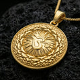 Load image into Gallery viewer, Gold plated Om pendant with detailed sacred symbol, circular sunburst center, and ornate geometric border showcased on black volcanic rock in a refined macro jewelry image

